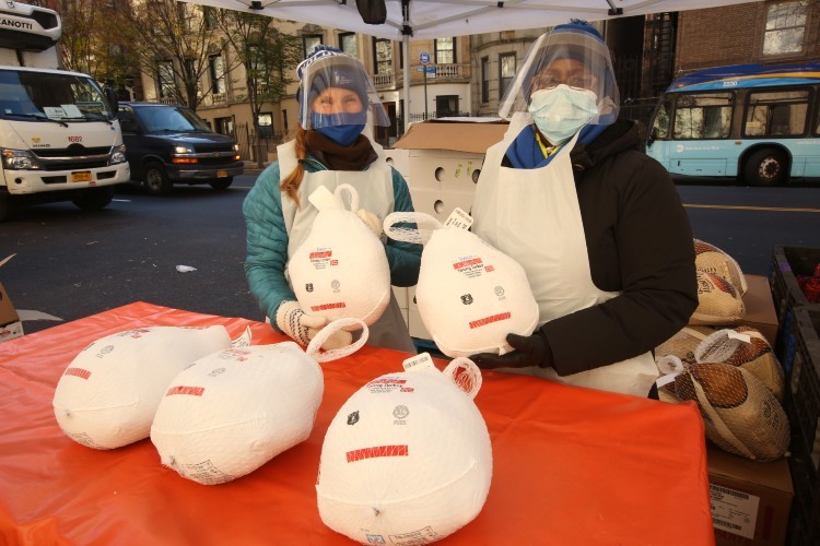 Two volunteers in masks and face shields hold turkeys up for the camera.