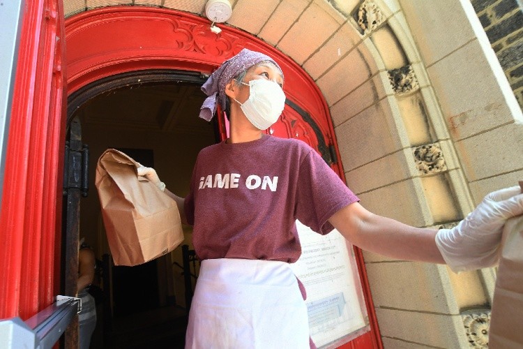 Woman with bag infront of door wearing mask.