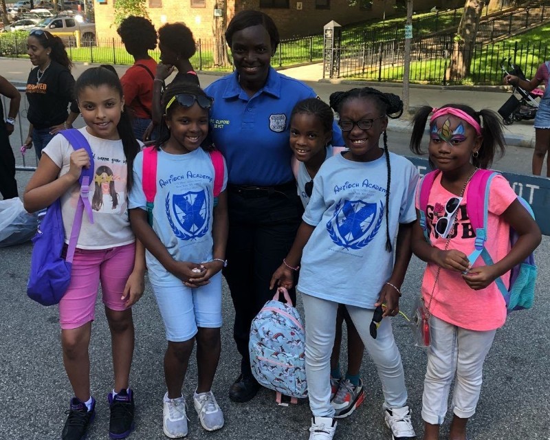 Police Officer with 5 girls with backpacks smiling.