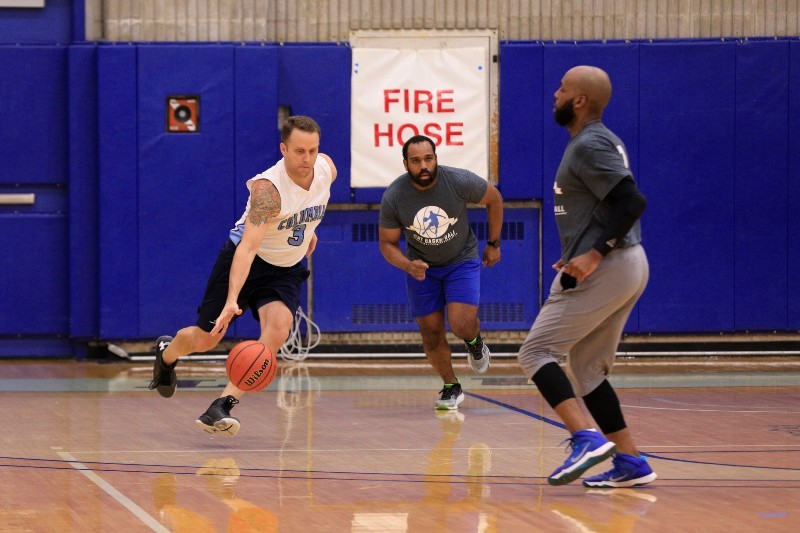 Three men playing basketball, with one dribbling past another.