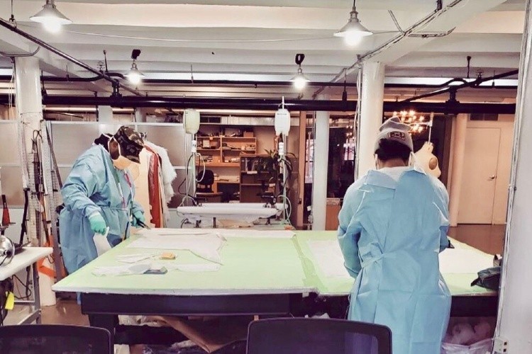 People in PPE working at desks, cutting textiles.